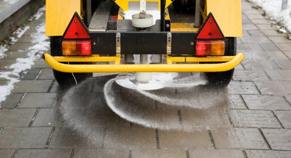 A machine is sprinkling salt on a sidewalk